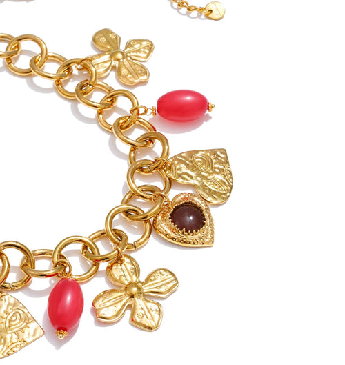 Gold charm bracelet with red beads on a white background
