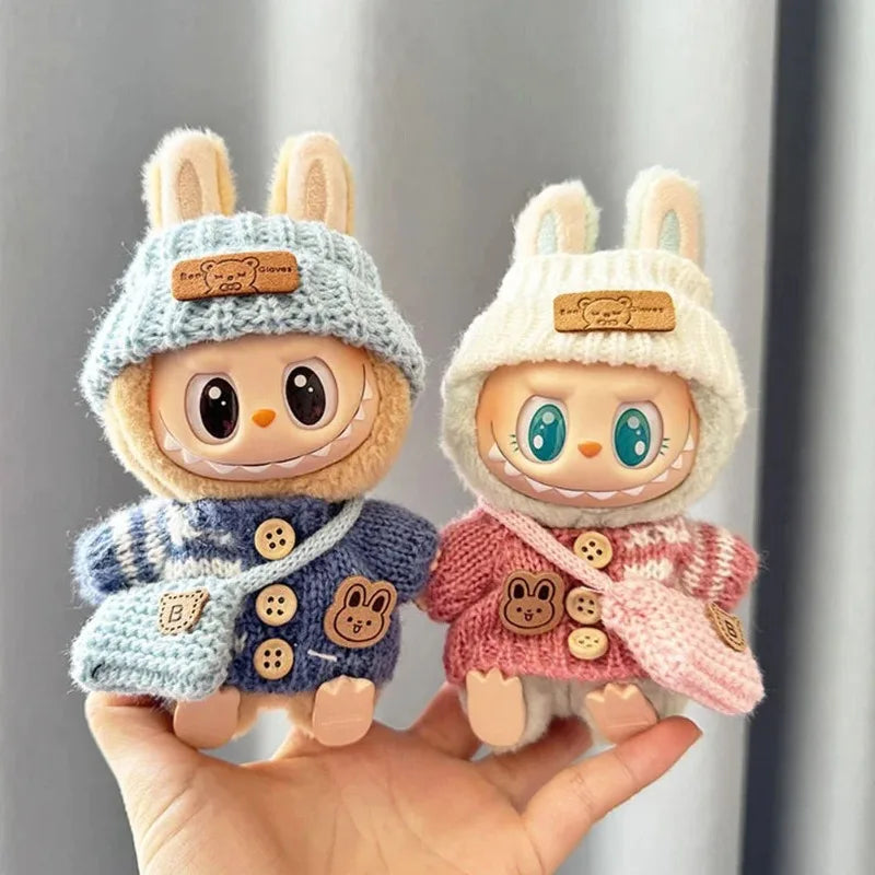 Two cute labubu plush toys with knitted hats and coats held in a hand against a neutral background.