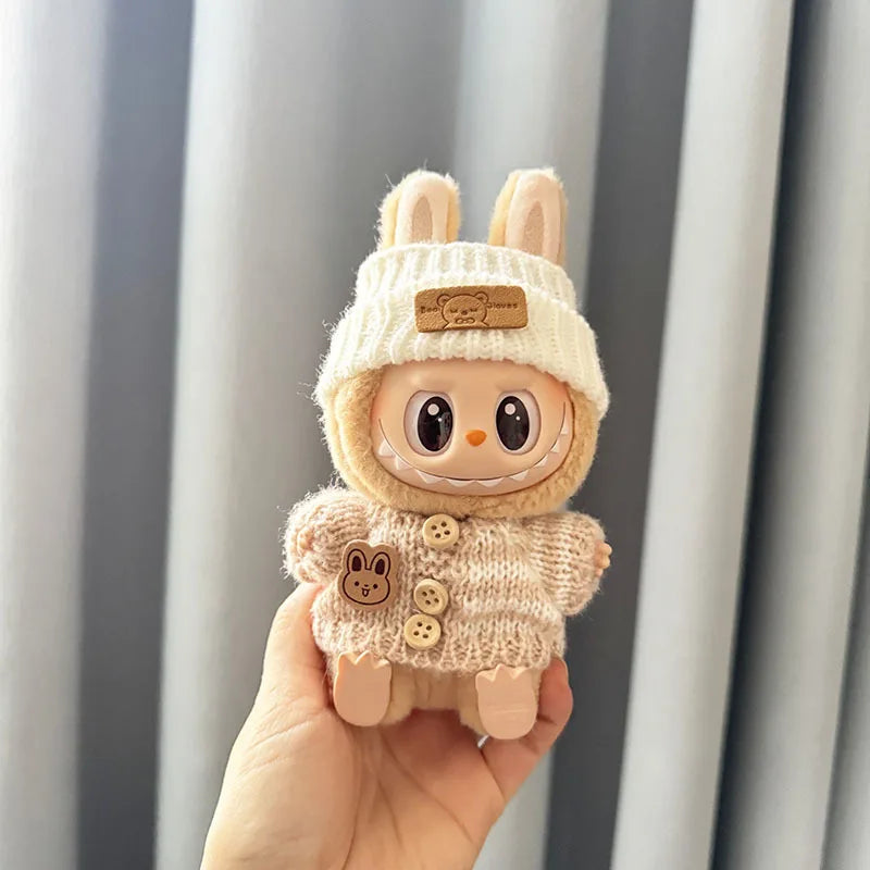 Plush labubu toy with a knitted hat and coat held in front of a striped curtain