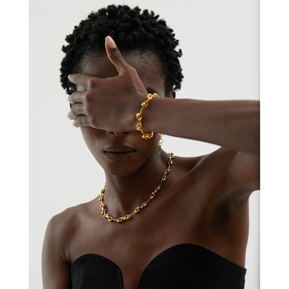 Person wearing a gold chain necklace and bracelet on a plain background