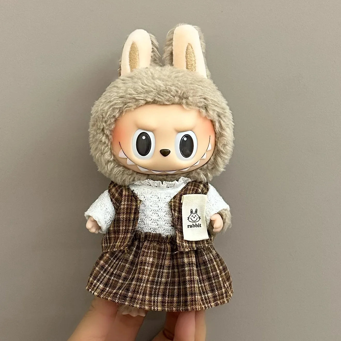 Labubu toy figure with rabbit ears and a plaid skirt on a plain background