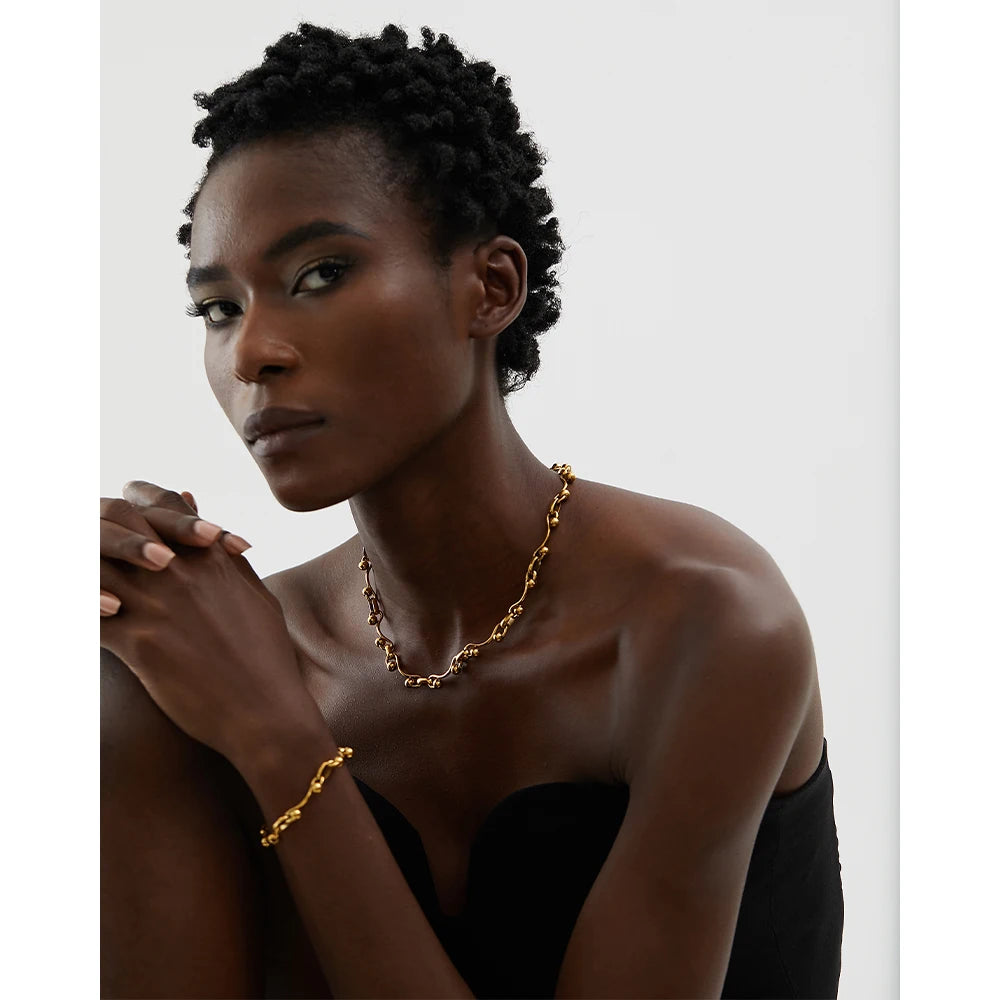 Woman wearing a gold necklace and bracelet against a plain background
