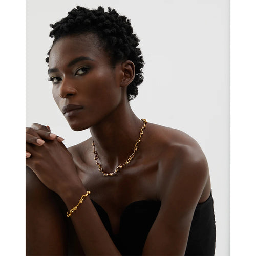 Woman wearing a gold necklace and bracelet against a plain background