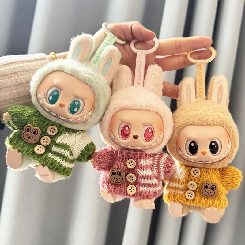 Three labubu plush keychains shaped like cartoon characters with bunny ears, wearing colorful sweaters, held against a neutral background.