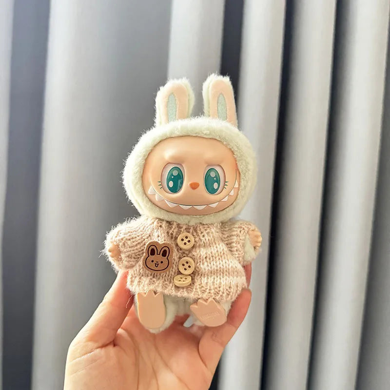 Plush labubu toy with bunny ears and sweater held in front of a neutral background