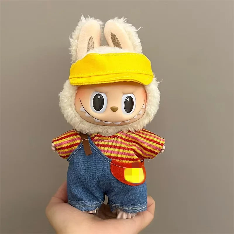 Plush Labubu  toy with bunny ears, yellow cap, striped shirt, and denim overalls held against a plain background.