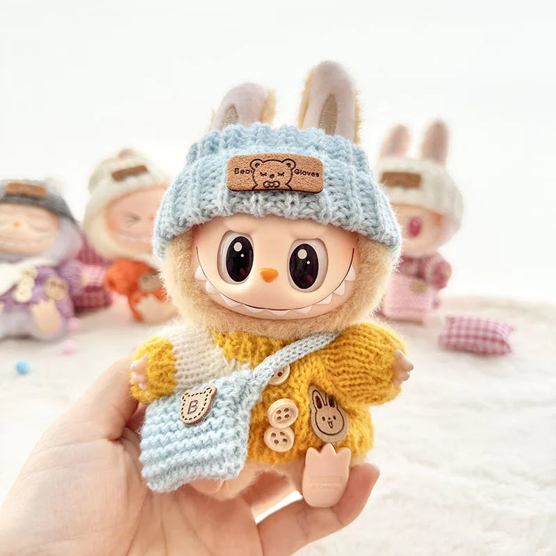 Labubu toy figure with a blue hat and yellow outfit held in a hand, with more figures in the background.