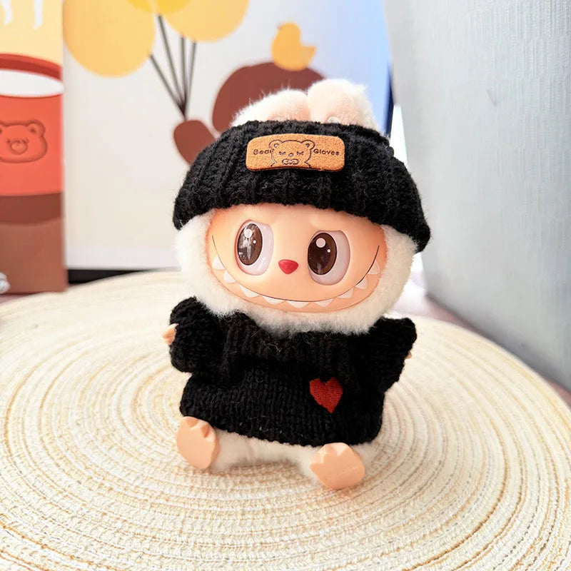 Plush labubu toy with a black hat and sweater on a textured surface