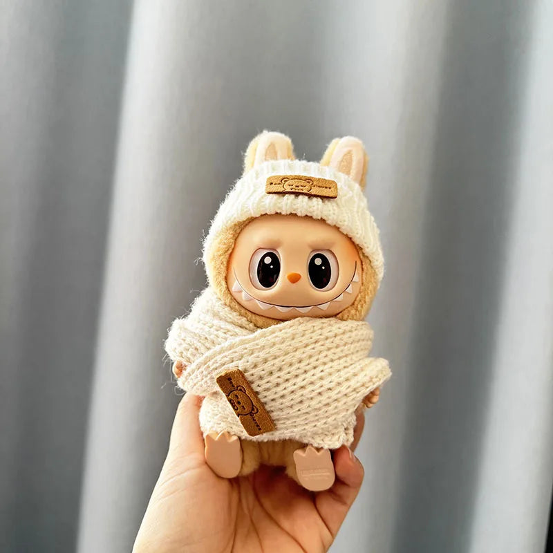 Labubu Toy resembling a baby alpaca in a knitted outfit held against a gray background