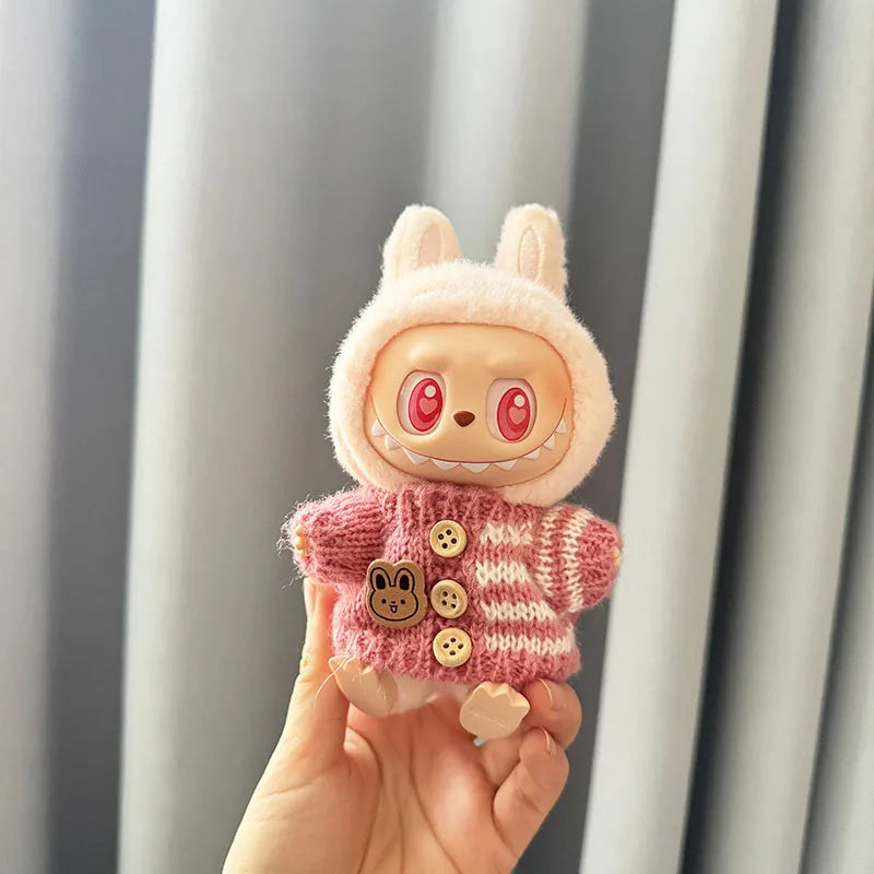 Labubu toy figure with bunny ears and a pink sweater held in a hand against a neutral background