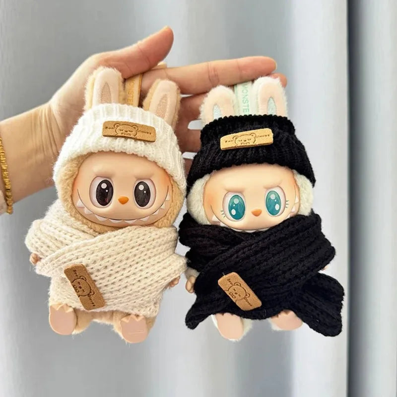 Two labubu plush toys with knitted hats and scarves held by a hand against a neutral background.