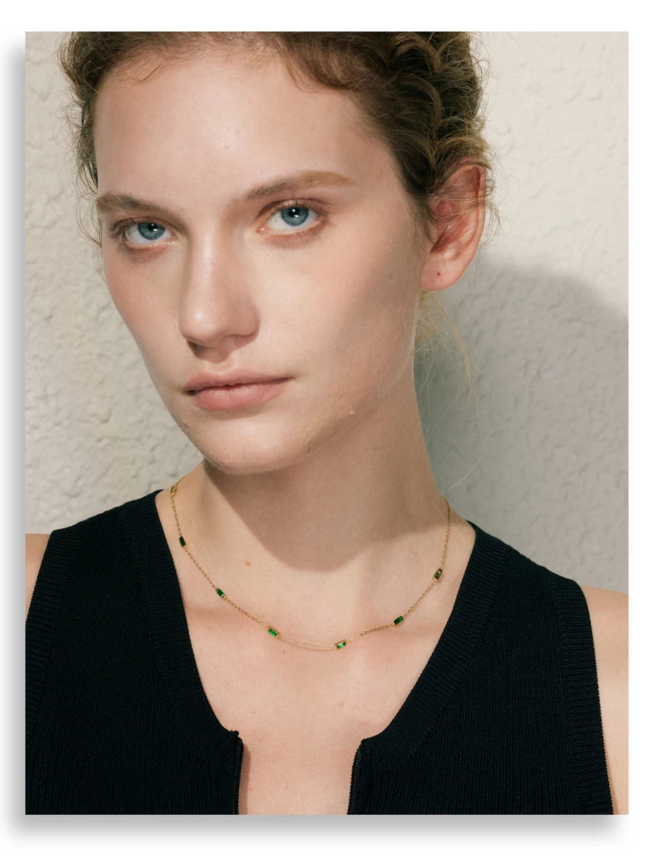 Woman wearing a black top and green necklace against a neutral background