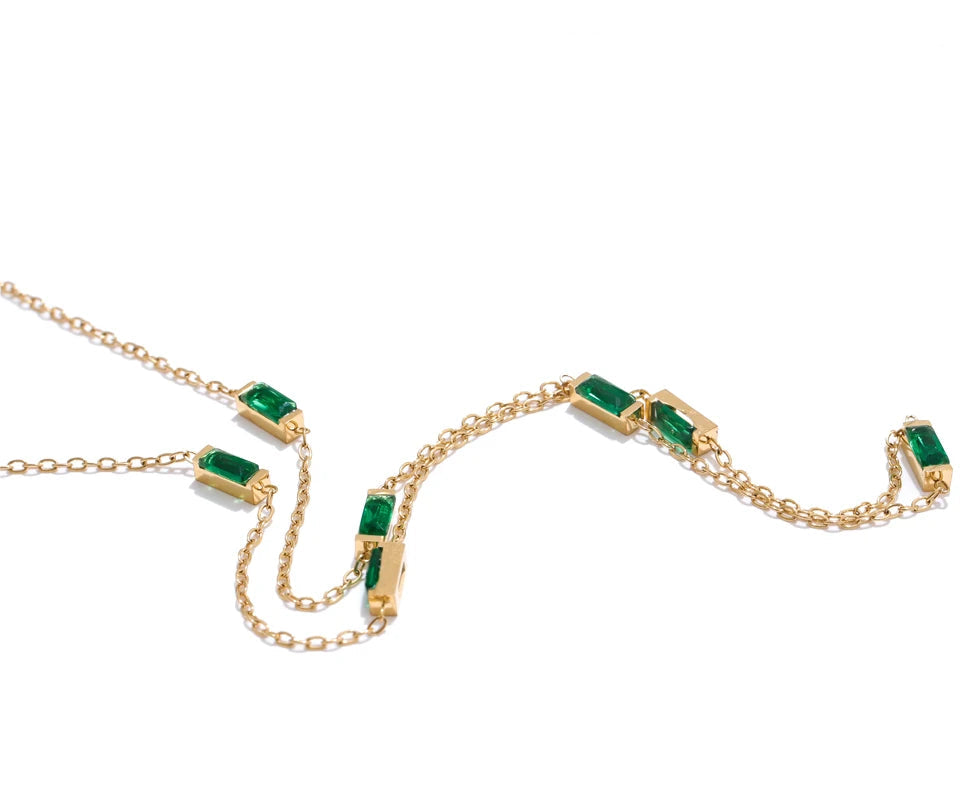 Gold necklace with emerald green gemstones on a white background