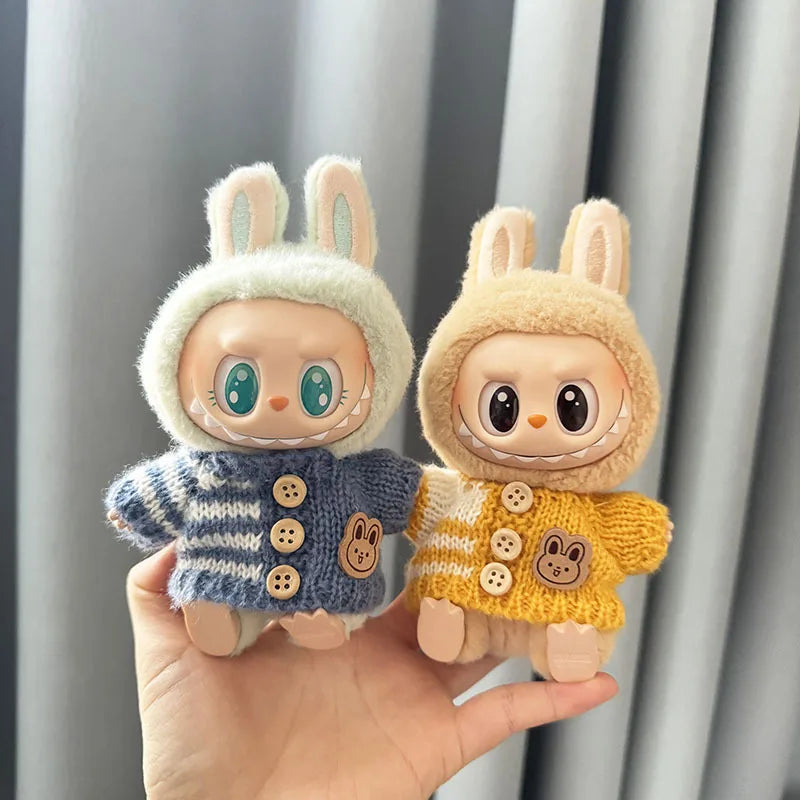 Two labubu plush toys with bunny ears and knitted sweaters held in a hand against a neutral background.