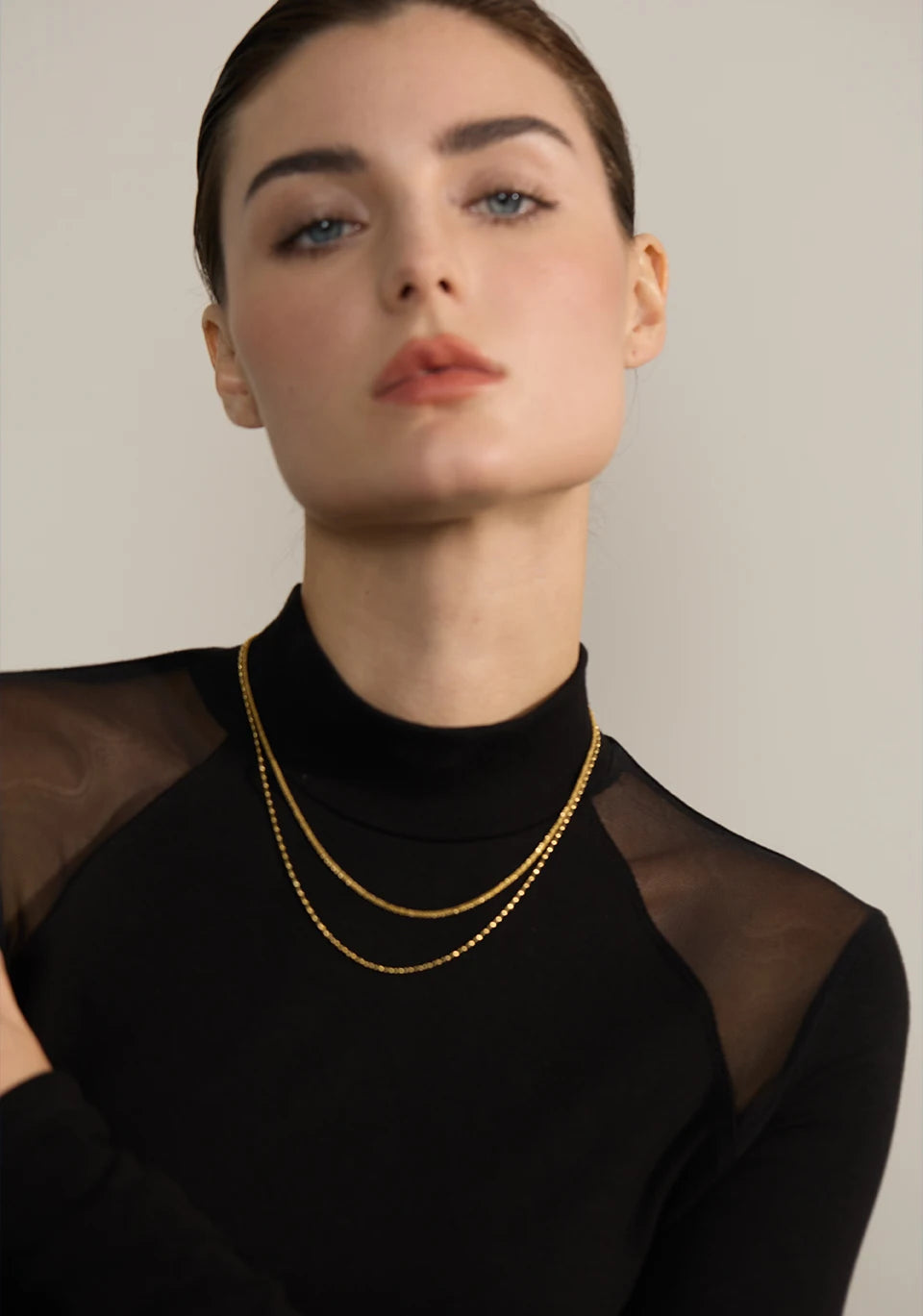 Woman wearing a gold necklace against a neutral background
