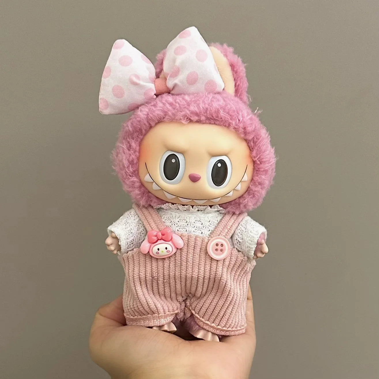 Labubu toy figure with pink hair and outfit held against a plain background