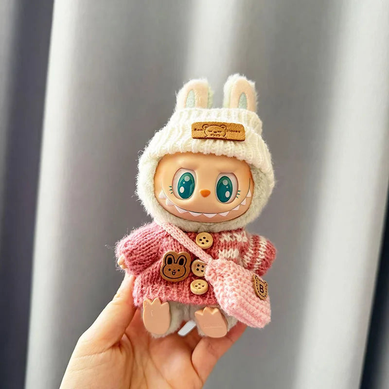 Labubu Toy figure of a character in a bunny costume with a pink sweater held by a hand against a neutral background.