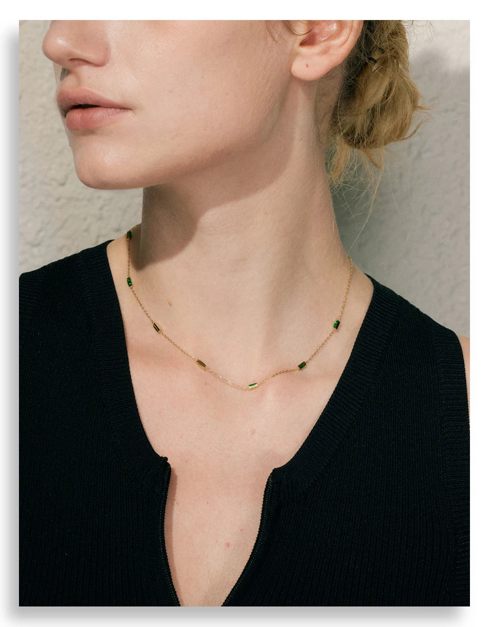 Person wearing a delicate necklace with green stones against a neutral background