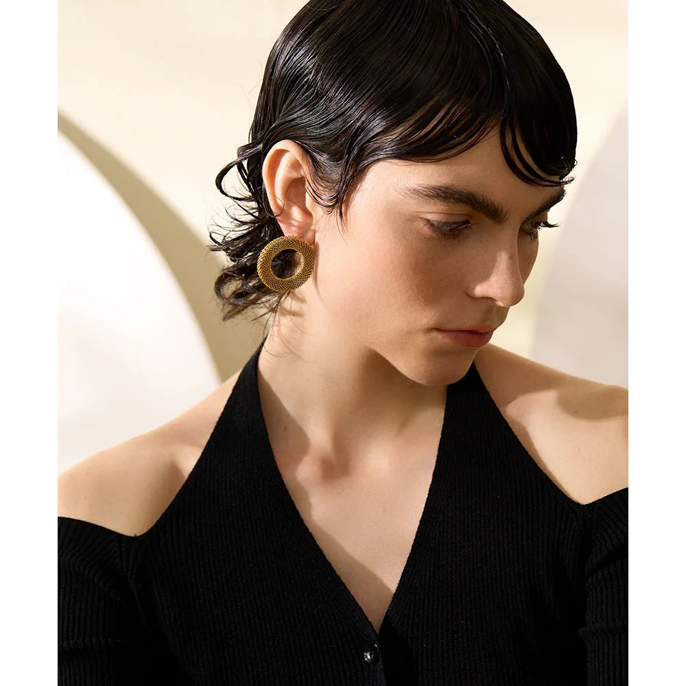 Close-up of a person wearing gold hoop earrings with a neutral background