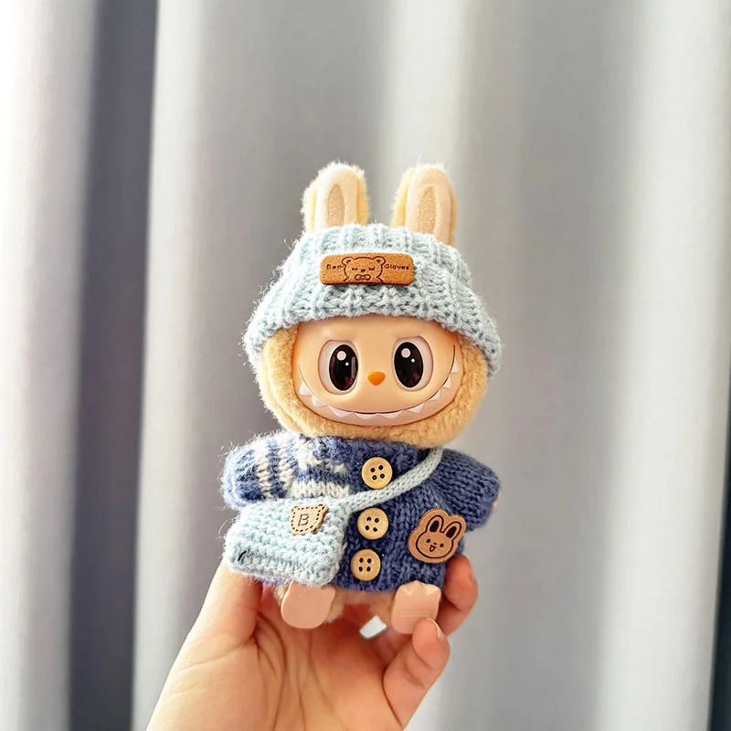 Small labubu plush toy with a blue knitted outfit and bunny ears held in a hand against a neutral background